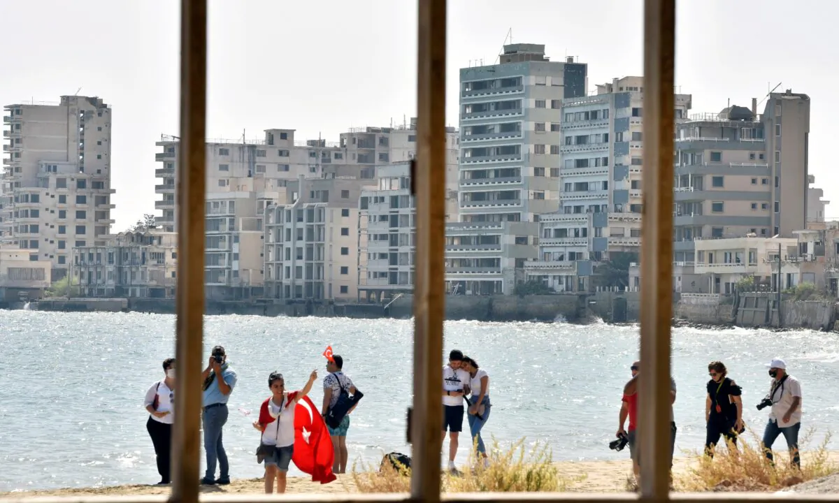People walk on a beach inside an area fenced off by the Turkish military since 1974 in the abandoned coastal area of Varosha, a suburb of the town of Famagusta in Turkish-controlled northern Cyprus, on Oct. 8, 2020. (Harun Ucar/Reuters)