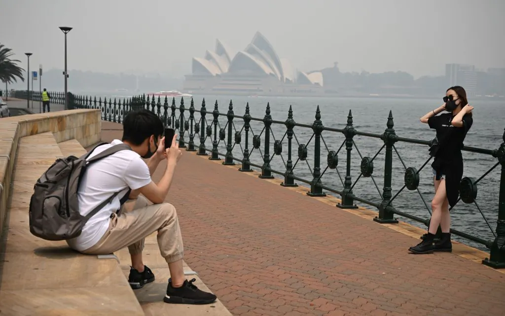 Tourists wearing masks take photos as the Opera House (back, C) is enveloped in haze caused by nearby bushfires, in Sydney on December 10, 2019. (PETER PARKS/Getty Images)