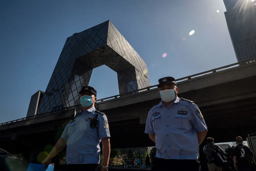 Police officers wearing masks walk as the CCTV Building, the headquarters for the Chinese regime's mouthpiece broadcaster, is seen in Beijing on May 19, 2020. (Nicolas Asfouri/AFP via Getty Images)