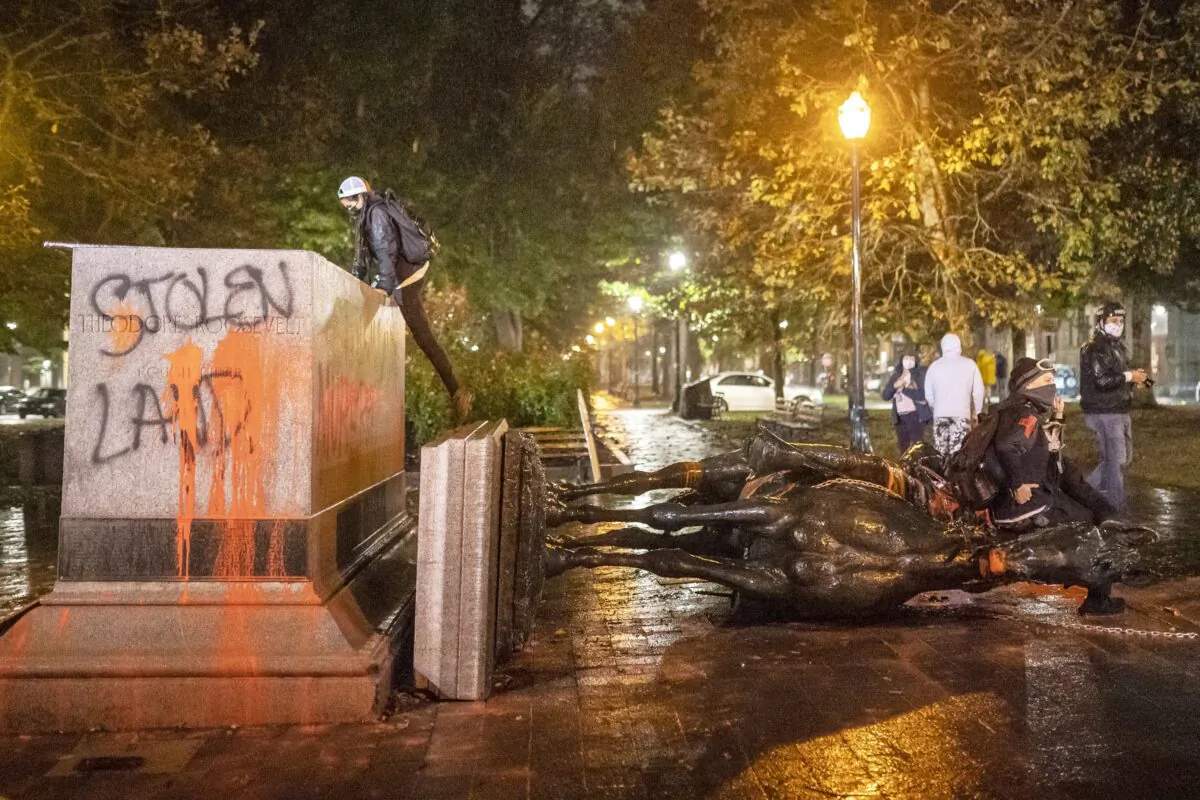 People stand near the toppled statue of President Theodore Roosevelt during a riot in Portland, Ore., Oct. 11, 2020. (Nathan Howard/Getty Images)