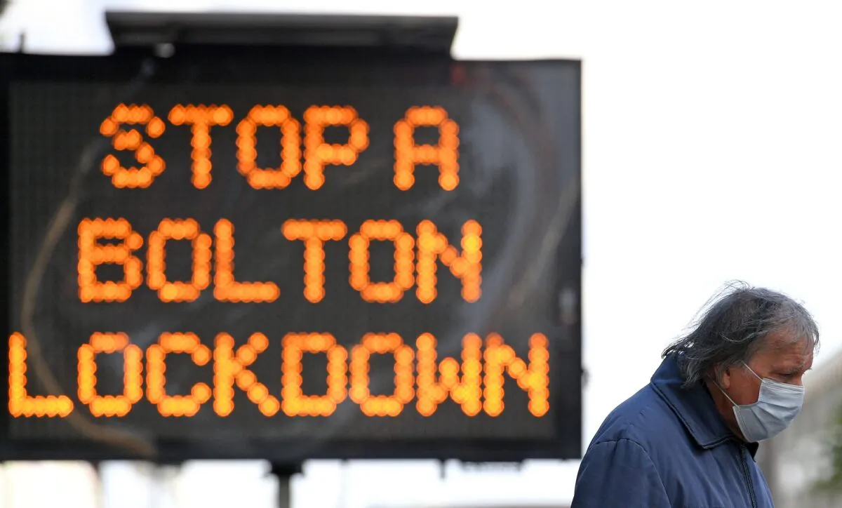 A man wearing a mask walks near an electronic road sign reading "Stop a Bolton Lockdown" in Bolton town centre, northwest England, on Oct. 7, 2020. (Oli Scarff/AFP via Getty Images)