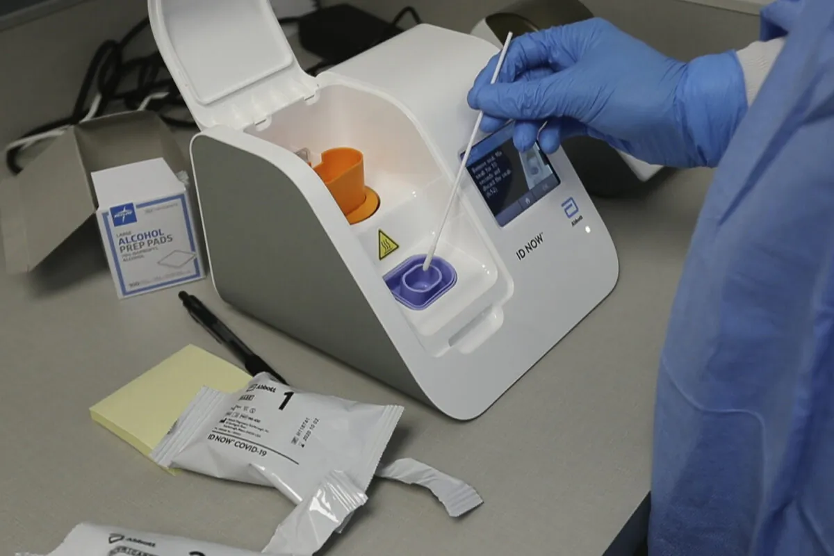 FILE - In this April 10, 2020, file frame grab from video, a lab technician dips a sample into the Abbott Laboratories ID Now testing machine at the Detroit Health Center in Detroit. Illinois-based Abbott Laboratories says its cartridge-based test, approved last month, delivers results within minutes. (AP Photo/Carlos Osorio)