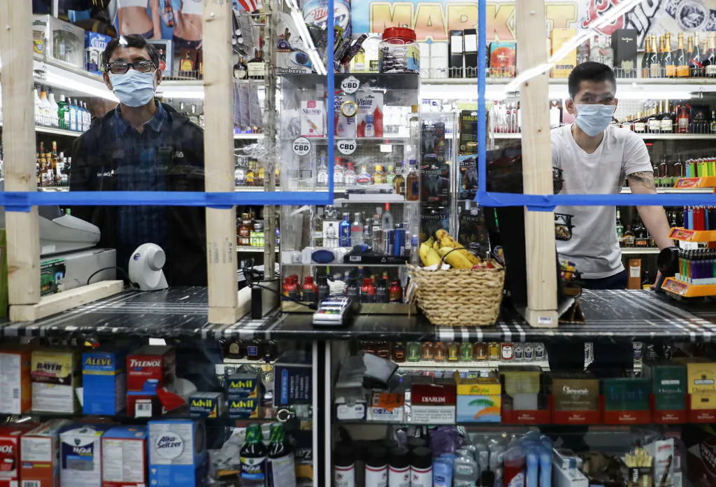 Cashiers wear face masks as they stand behind newly installed plexiglass barriers for protection in a liquor store amid the COVID-19 pandemic in Los Angeles, Calif., on April 4, 2020. (Mario Tama/Getty Images)