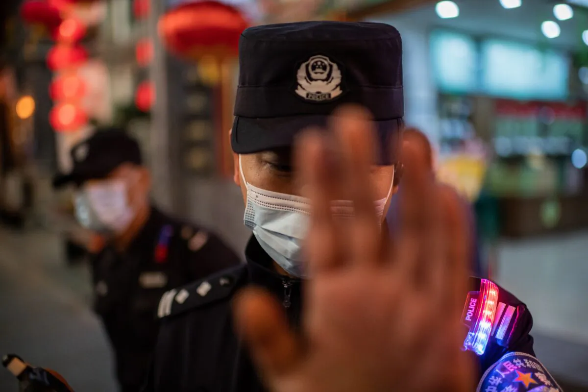A police officer wearing a face mask tries to stop a photojournalist taking pictures on a street outside of a shopping mall complex in Beijing on Oct. 13, 2020. (Nicolas Asfouri/AFP via Getty Images)
