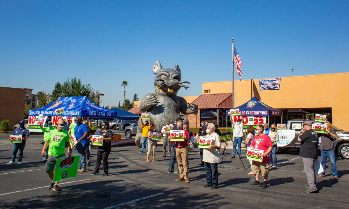 Workers stand in unison holding signs at a rally opposing Proposition 22, a measure that would allow ride-share drivers to work as independent contractors, in Orange, Calif., on Oct. 16, 2020. (John Fredricks/The Epoch Times) 