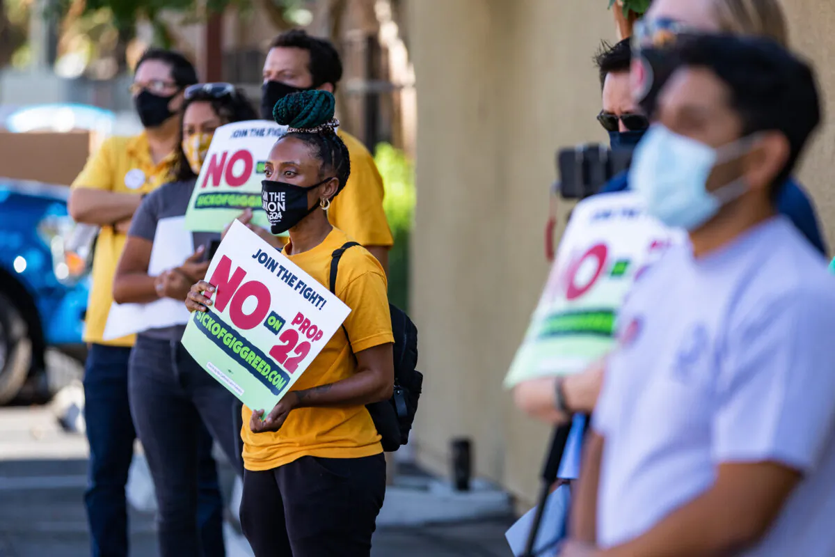 Workers hold signs calling for onlookers to vote against Proposition 22 at a gathering in Orange, Calif., on Oct. 16, 2020. (John Fredricks/The Epoch Times)