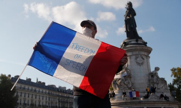 A demonstrator holds a French flag with the slogan _Freedom of Speech_