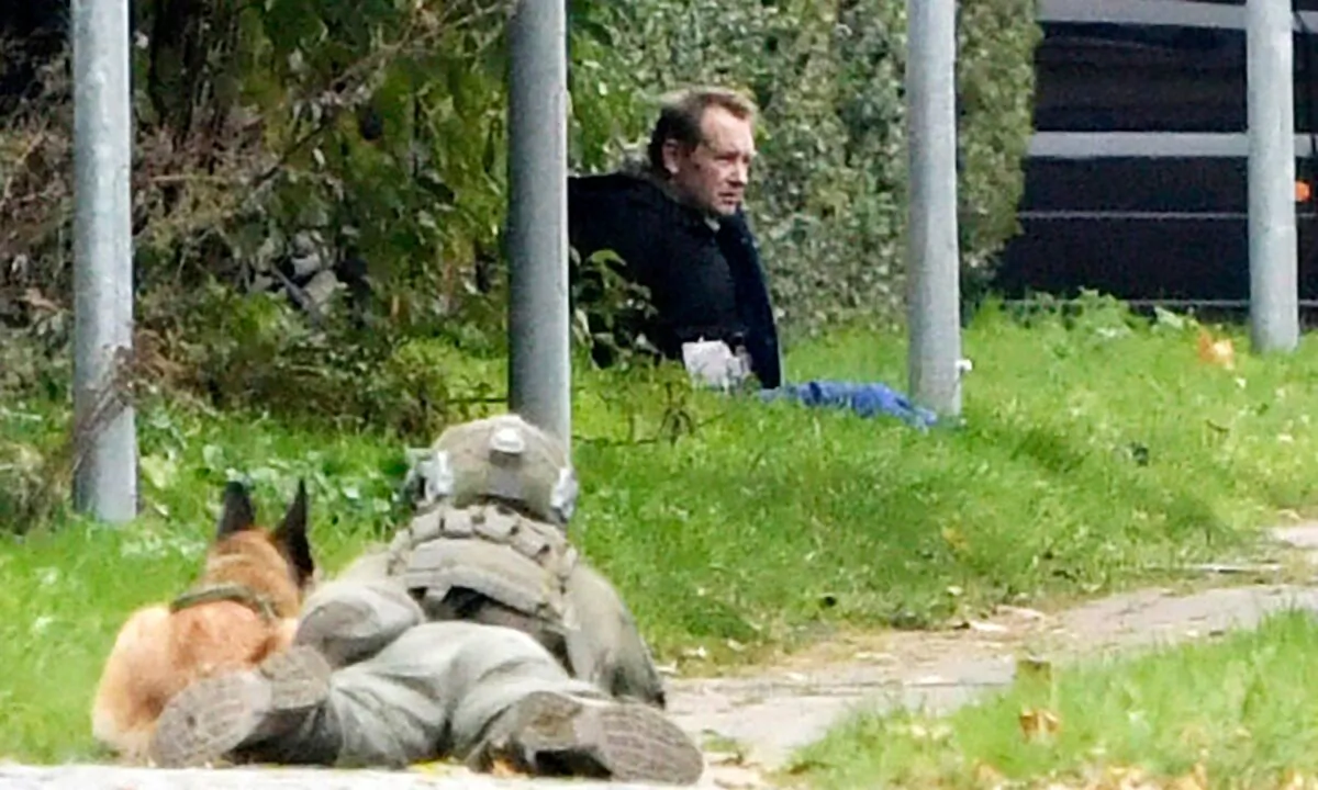 A police officer watches Peter Madsen as he sits on the side of a road after being apprehended following a failed escape attempt in Albertslund, Denmark, on Oct. 20, 2020. The self-taught Danish engineer, who was convicted of torturing and murdering a Swedish journalist on his homemade submarine in 2017 before dismembering her body and dumping it at sea, on Tuesday was captured after an attempted prison escape outside the suburban Copenhagen jail where he is serving life sentence. (Nils Meilvang/Ritzau Scanpix via AP)