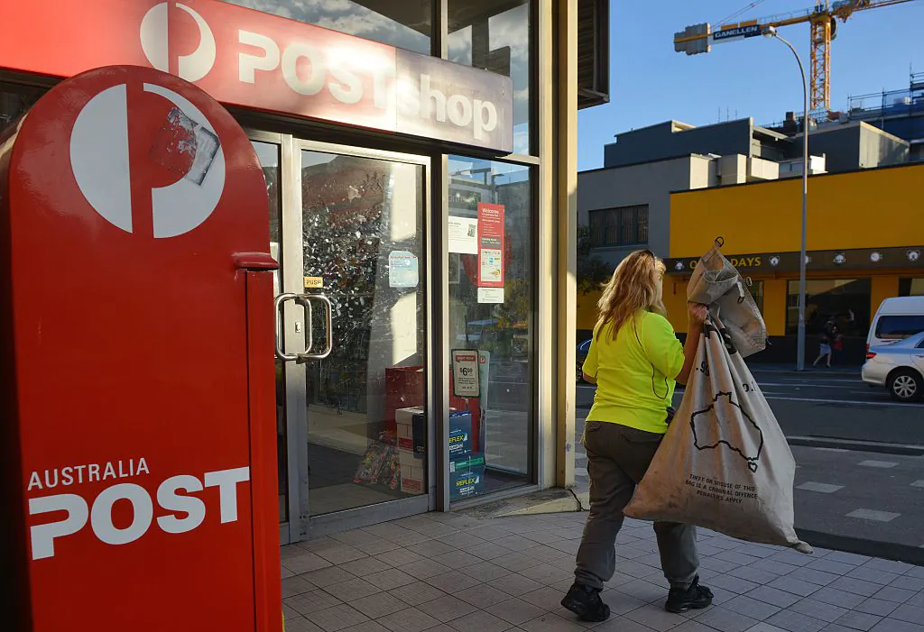 A worker carries a sack of letters after emptying a post box outside an Australia Post office in Sydney on June 26, 2015.  Australia Post was June 26 expected to axe hundreds of jobs as it struggles with growing losses from a decline in letter volumes despite growth in its parcels business.     AFP PHOTO / Peter PARKS        (Photo credit should read PETER PARKS/AFP via Getty Images)