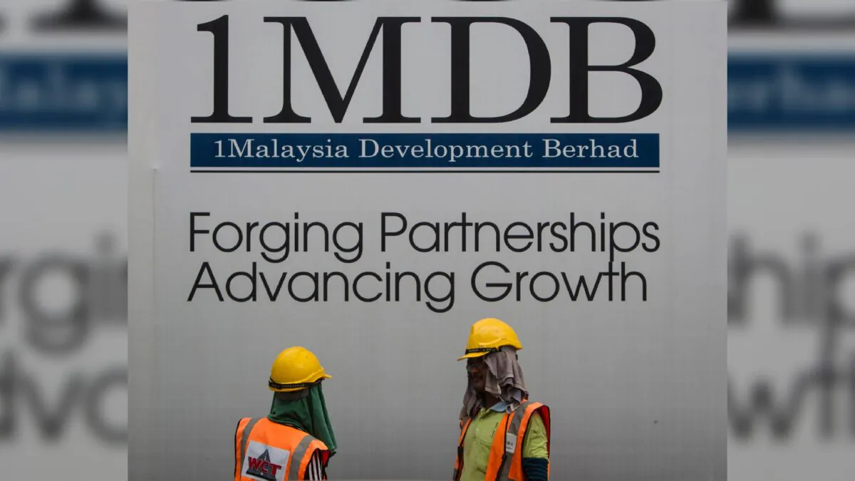 Construction workers chat in front of a billboard for state investment fund 1 Malaysia Development Berhad (1MDB) at the fund's flagship Tun Razak Exchange development in Kuala Lumpur, Malaysia, on May 14, 2015. (Joshua Paul/AP Photo)