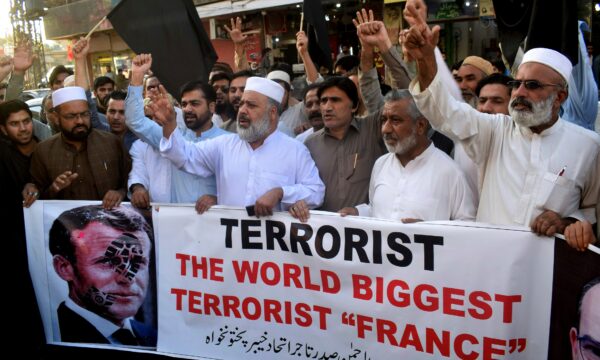 Pakistan traders hold a banner with a defaced picture of French President Emmanuel Macron
