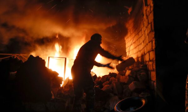 People try to remove car tyres from a car shop on fire