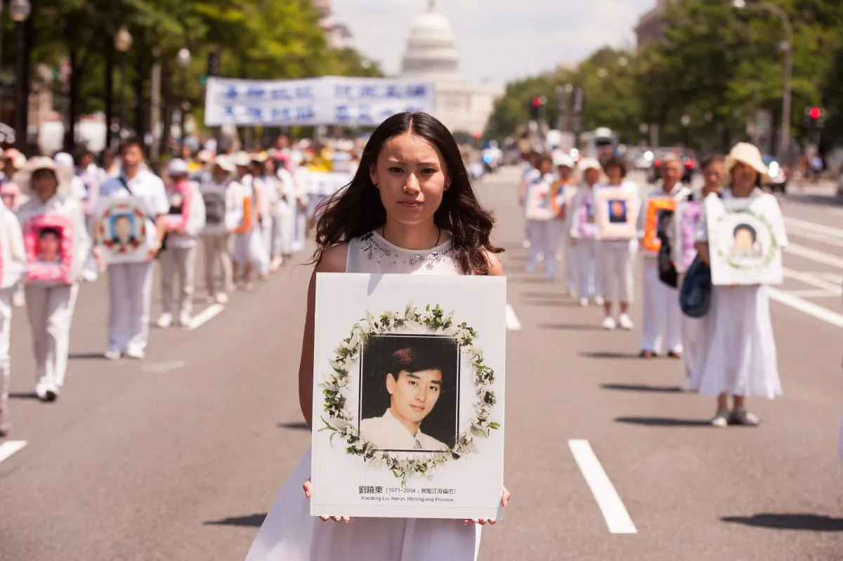 A woman holds a photo of a man killed by the Chinese regime in its persecution of Falun Gong, during a parade in Washington on July 17, 2014. (Larry Dye/The Epoch Times)