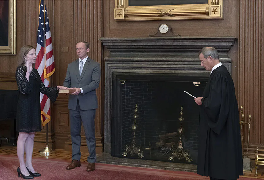 Chief Justice John G. Roberts, Jr., administers the Judicial Oath to Judge Amy Coney Barrett in the East Conference Room, Supreme Court Building. Judge Barrett’s husband, Jesse M. Barrett, holds the Bible.  
(Fred Schilling, Collection of the Supreme Court of the United States)