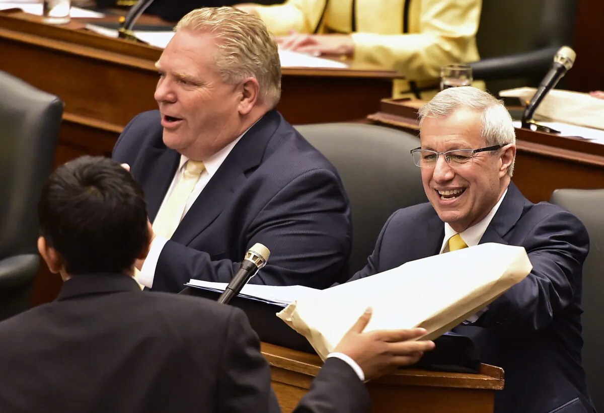 Ontario Finance Minister Vic Fedeli (R) is handed a copy of the 2019 budget as Premier Doug Ford looks on at the legislature in Toronto on April 11, 2019. (Frank Gunn/The Canadian Press)
