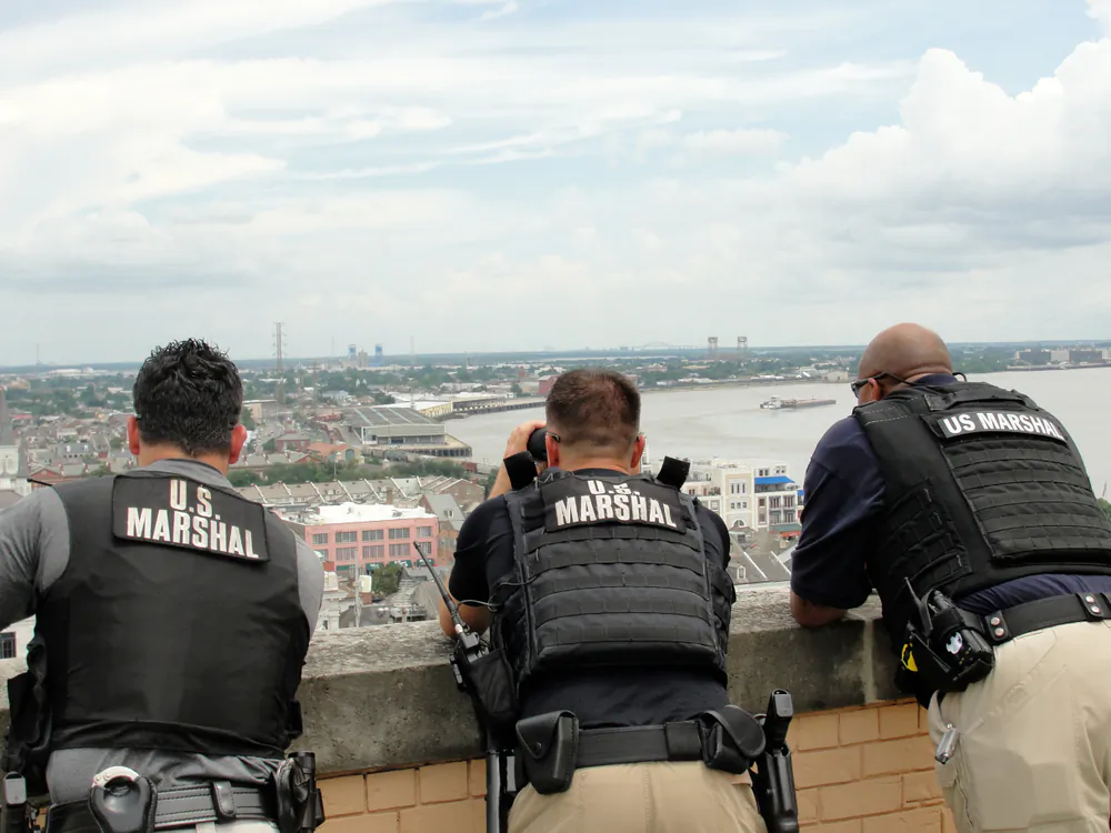 U.S. Marshals stand on a building as they look out toward the city in a file photo. (Illustration - Elliott Cowand Jr/Shutterstock)