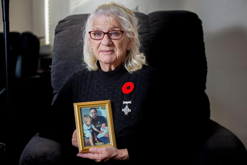 Debbie Sullivan holds a photo of her son Christopher Saunders and his two sons while wearing her National Silver Cross at her home in Summerville, New Brunswick, Canada, on Oct. 31, 2020. (James West/The Canadian Press)