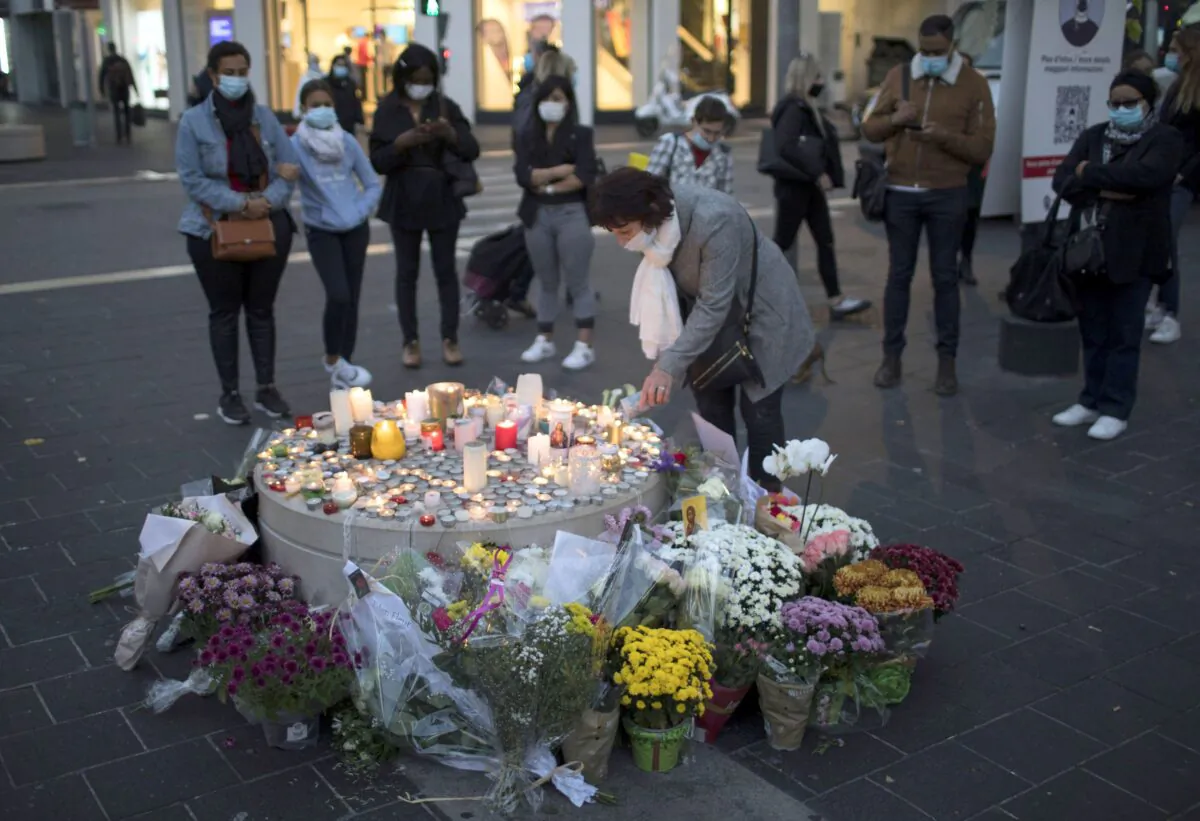 A woman lights a candle in front of the Notre-Dame Basilica in Nice, France, on Oct. 30, 2020. A man stabbed three people to death in the church on Oct. 29. (AP Photo/Daniel Cole)