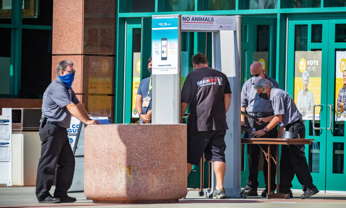 Security personnel watch a man pass through a metal detector as he prepares to enter a temporary voting center set up inside the Honda Center in Anaheim, Calif., on Nov. 2, 2020. (John Fredricks/The Epoch Times)