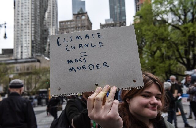 A woman holds a sign saying "climate change = mass murder" while people participate in a a protest with a group called Extinction Rebellion in New York City on April 17, 2019. (Stephanie Keith/Getty Images)