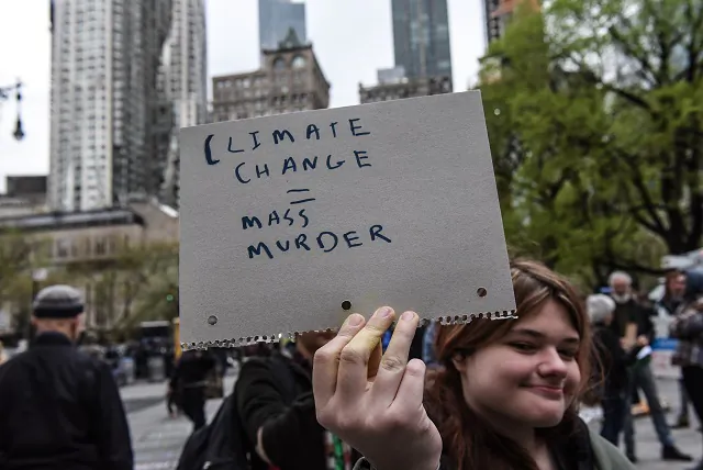 A woman holds a sign saying "climate change = mass murder" while people participate in a a protest with a group called Extinction Rebellion in New York City on April 17, 2019. (Stephanie Keith/Getty Images)