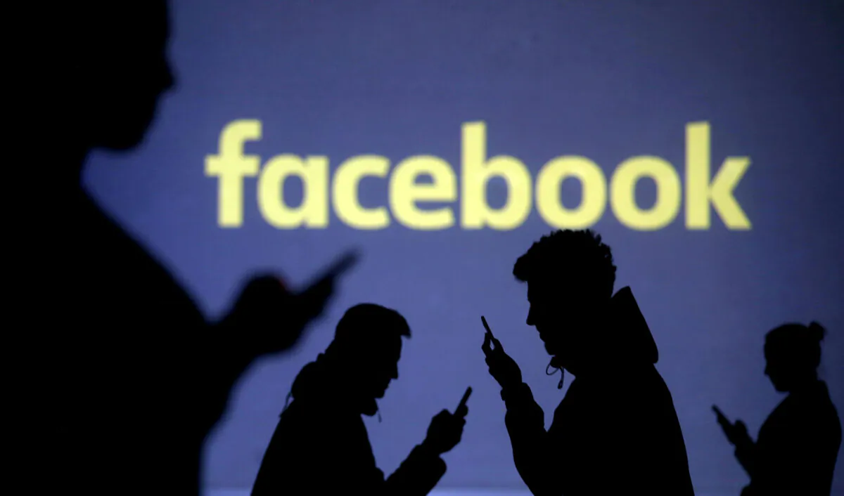 Silhouettes of mobile users are seen next to a screen projection of Facebook logo in this picture illustration taken March 28, 2018. (Dado Ruvic/Reuters)