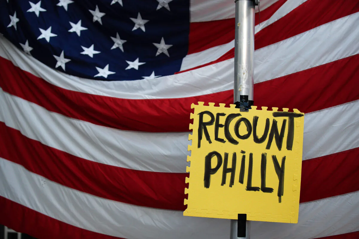 A sign hangs in front of an American flag, as supporters of President Donald Trump protest outside the Pennsylvania Convention Center, in Philadelphia, on Nov. 10, 2020. (Rebecca Blackwell/AP Photo)
