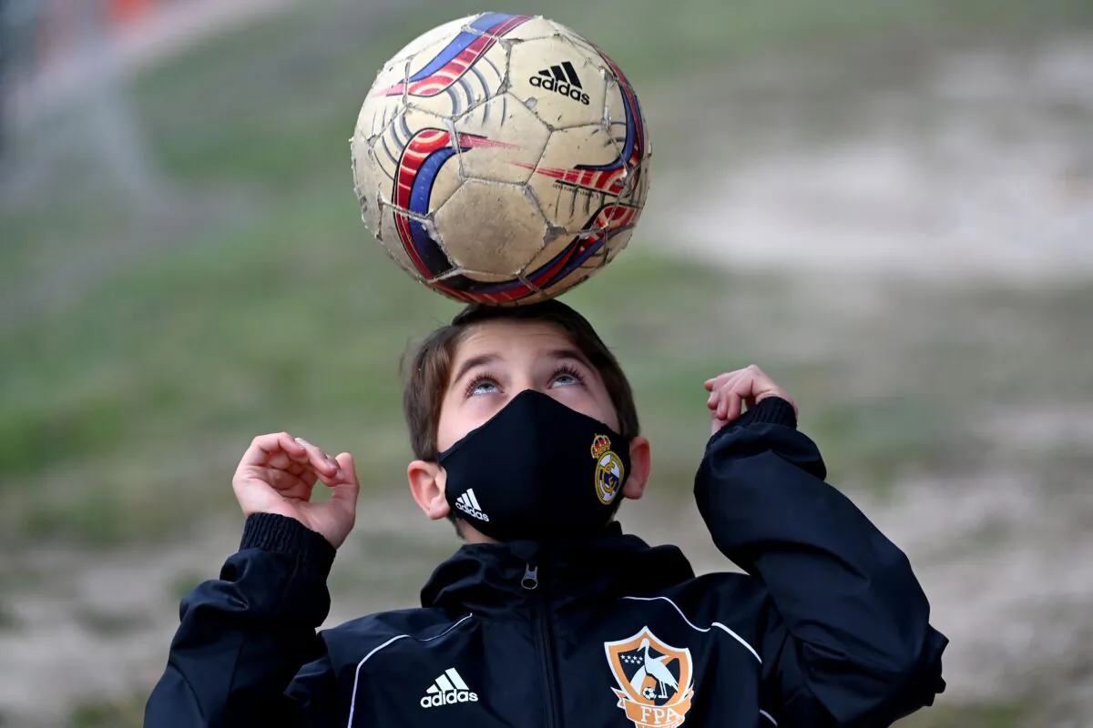 A boy wearing a face mask to protect against the spread of the novel coronavirus juggles with a ball prior to a football match with his team of Football Player Academy (FPA) Las Rozas in Las Rozas, near Madrid, on Oct. 24, 2020. (Gabriel Bouys/AFP via Getty Images) 