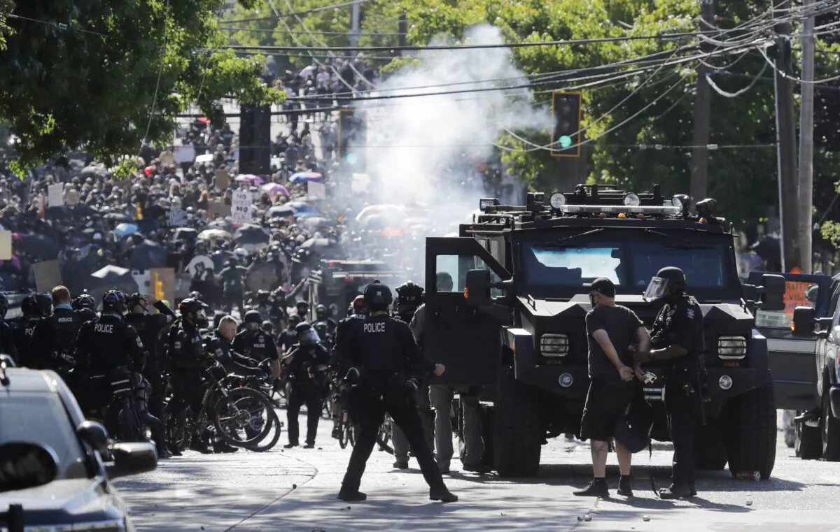 A man is arrested while smoke rises in the air as police and protesters clash near the Seattle Police East Precinct headquarters in Seattle on July 25, 2020. (AP Photo/Ted S. Warren)