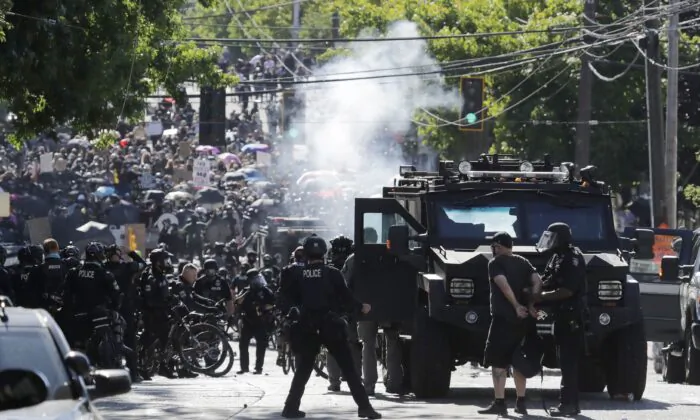 A man is arrested while smoke rises as police and protesters clash near the Seattle Police East Precinct headquarters in Seattle on July 25, 2020. (AP Photo/Ted S. Warren)