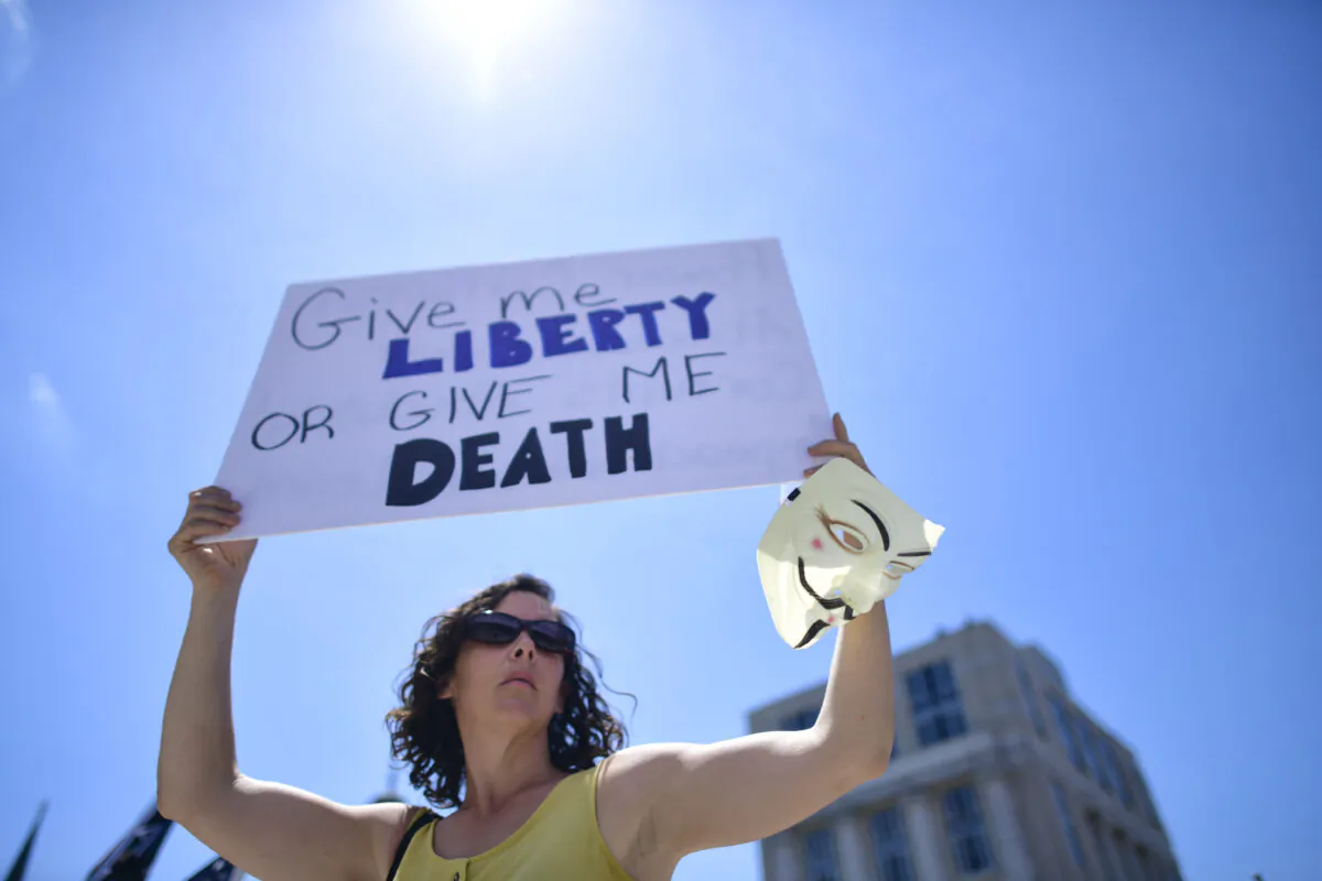 A woman holds a placard stating "Give me LIBERTY OR GIVE ME DEATH" while joining demonstrators at a rally outside the Pennsylvania Capitol Building to protest the continued closure of businesses due to the coronavirus pandemic in Harrisburg, Penn., on May 15, 2020. (Mark Makela/Getty Images)