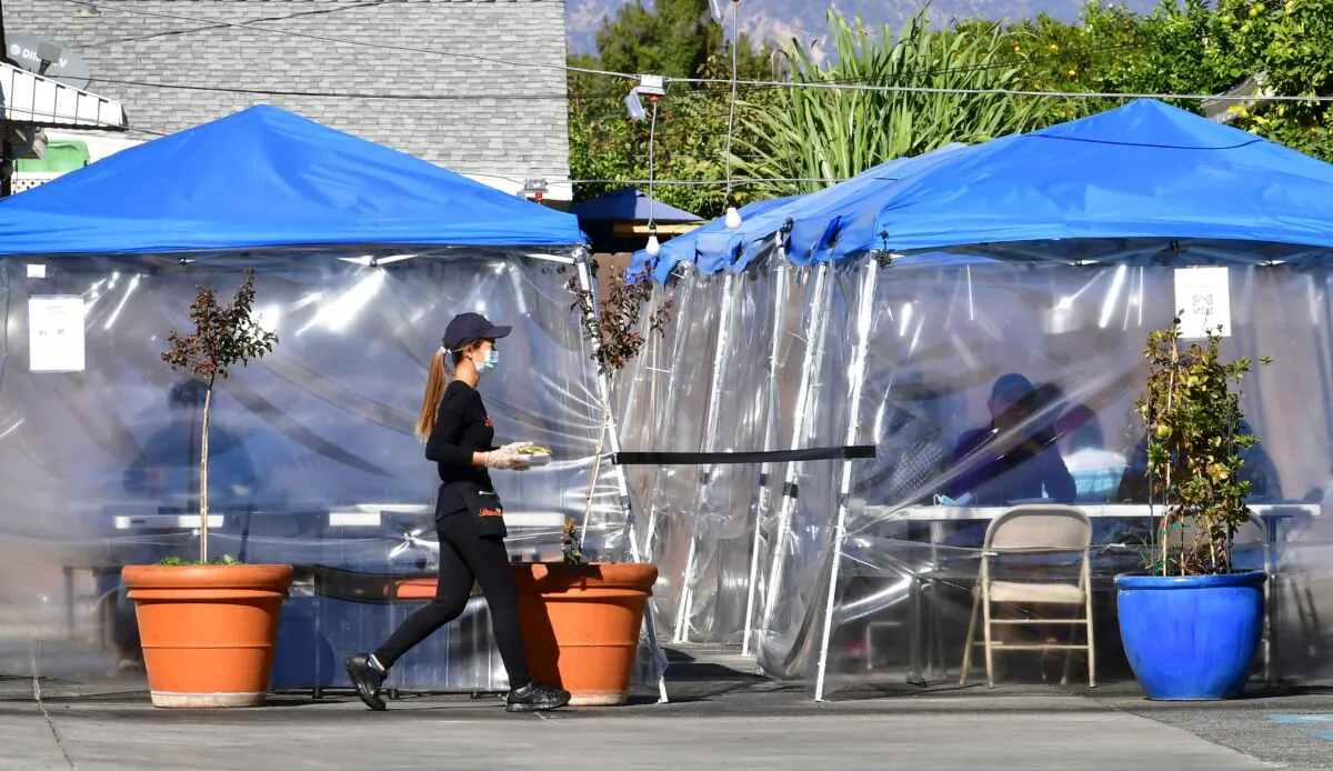 A waitress delivers orders to diners seated outdoors under tents in a restaurant's parking lot in Alhambra, Calif., on Nov. 17, 2020. (Frederic J. Brown/AFP via Getty Images)