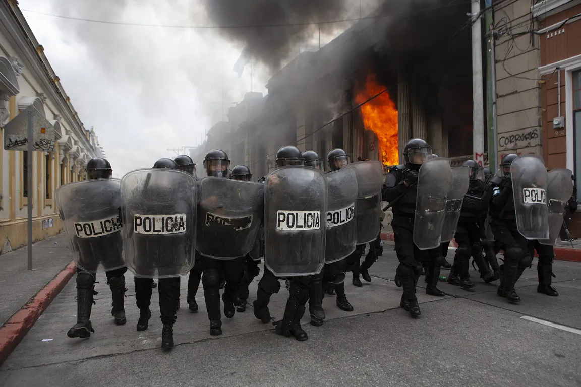Riot police form a cordon as flames shoot out from the Congress building after protesters set a part of the building on fire, in Guatemala City on Nov. 21, 2020. (AP Photo/Oliver De Ros)