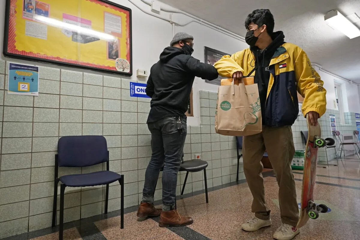 West Brooklyn Community High School principal Malik Lewis (L) bumps elbows with former student Jason Cardoso after Cardoso came to pick up the diploma he earned when he graduated in March, on Nov. 19, 2020, in the Brooklyn borough of New York. (Kathy Willens/AP Photo)