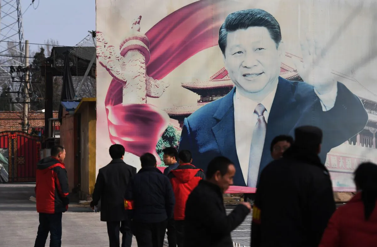 People stand near a faded propaganda billboard featuring an image of Chinese leader Xi Jinping, in a car park in Beijing on March 19, 2018. (Greg Baker/AFP via Getty Images)