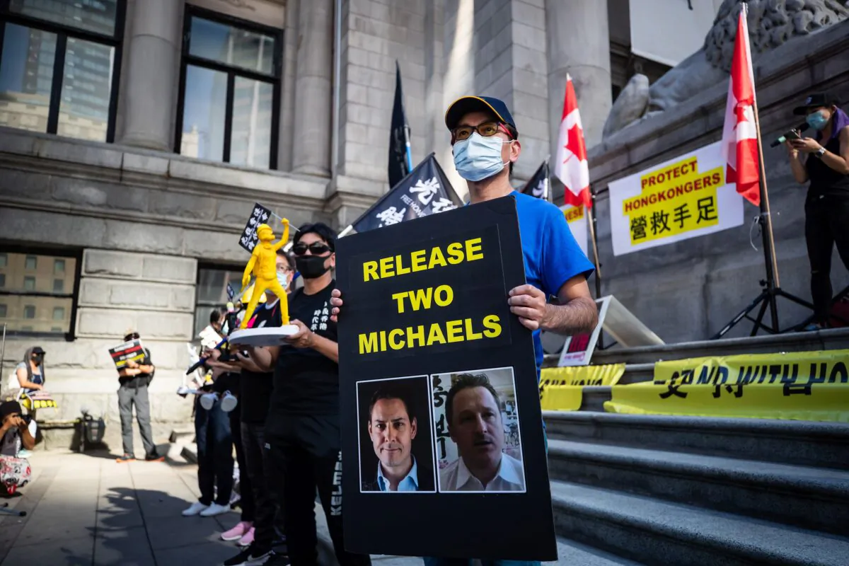 A man holds a sign with photographs of Michael Kovrig and Michael Spavor, who were detained in China in December 2018, as people gather for a rally in Vancouver in support of Hong Kong democracy on Aug. 16, 2020. (The Canadian Press/Darryl Dyck)