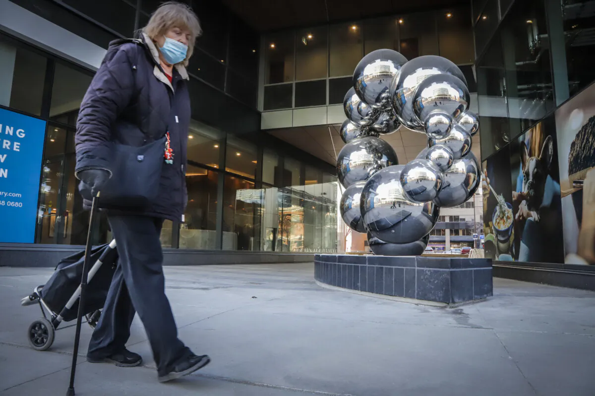 A woman wearing a mask walks past a sculpture in Calgary on Dec. 2, 2020. (Jeff McIntosh/The Canadian Press)