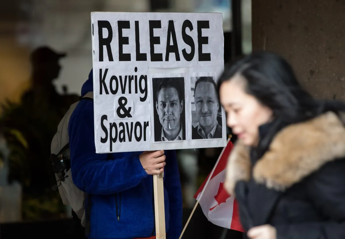 A young man holds a sign bearing photographs of Michael Kovrig and Michael Spavor, who have been detained in China for more than a year, outside B.C. Supreme Court where Huawei chief financial officer Meng Wanzhou was attending a hearing, in Vancouver, Canada, on Jan. 21, 2020. (Darryl Dyck/The Canadian Press)
