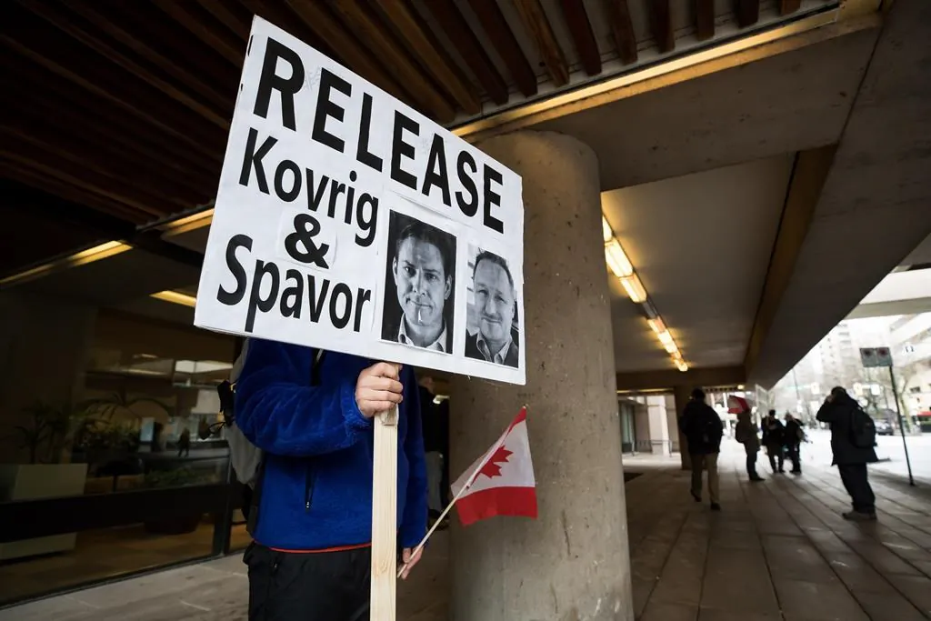 A young man holds a sign bearing photographs of Michael Kovrig and Michael Spavor, who have been detained in China for two years, outside B.C. Supreme Court during a hearing for  Huawei chief financial officer Meng Wanzhou on Jan. 21, 2020. (The Canadian Press/Darryl Dyck)