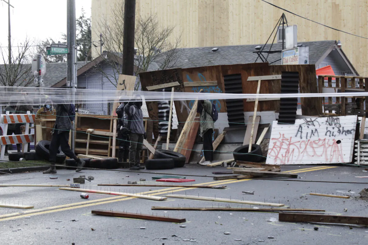Protesters stand behind barricades at their encampment outside a home in Portland, Ore., on Dec. 9, 2020. (AP Photo/Gillian Flaccus)