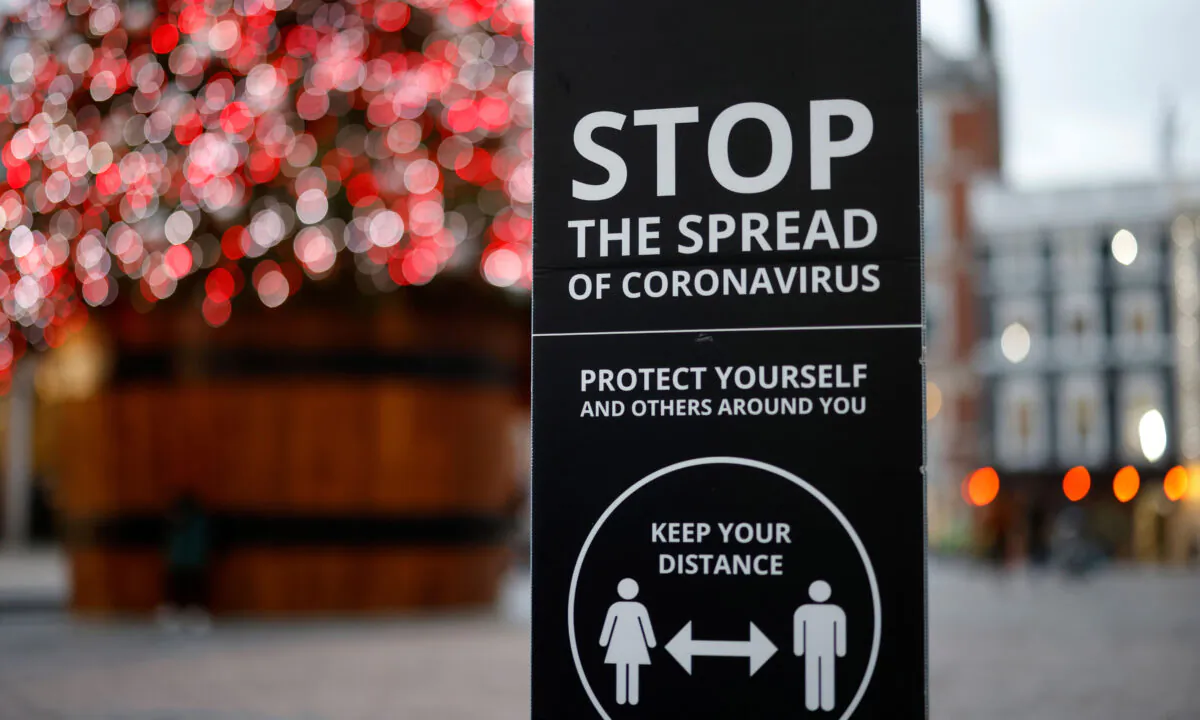 A sign promoting social distancing to combat the spread of the CCP virus is seen beside the Christmas tree in Covent Garden in central London on Nov. 27, 2020. (Tolga Akmen/AFP via Getty Images)