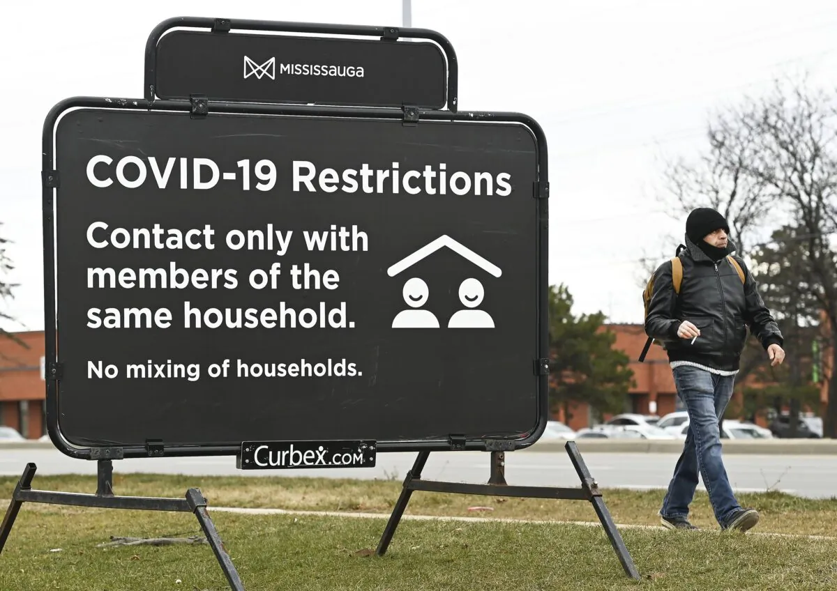 A man walks past a COVID-19 restrictions sign during the COVID-19 pandemic in Mississauga, Ont., on Dec. 22, 2020. (The Canadian Press/Nathan Denette)