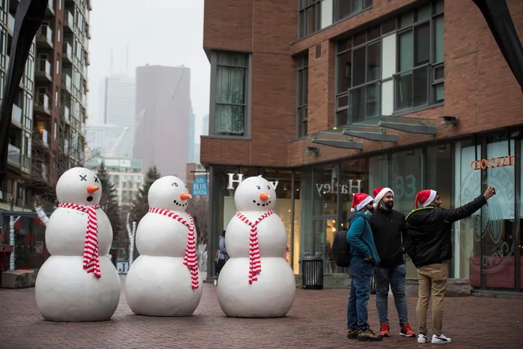 A group wearing Santa hats stop to take a selfie next to the snowmen display at the Distillery District in Toronto on Christmas Eve, Dec. 24, 2020. (The Canadian Press/Tijana Martin)