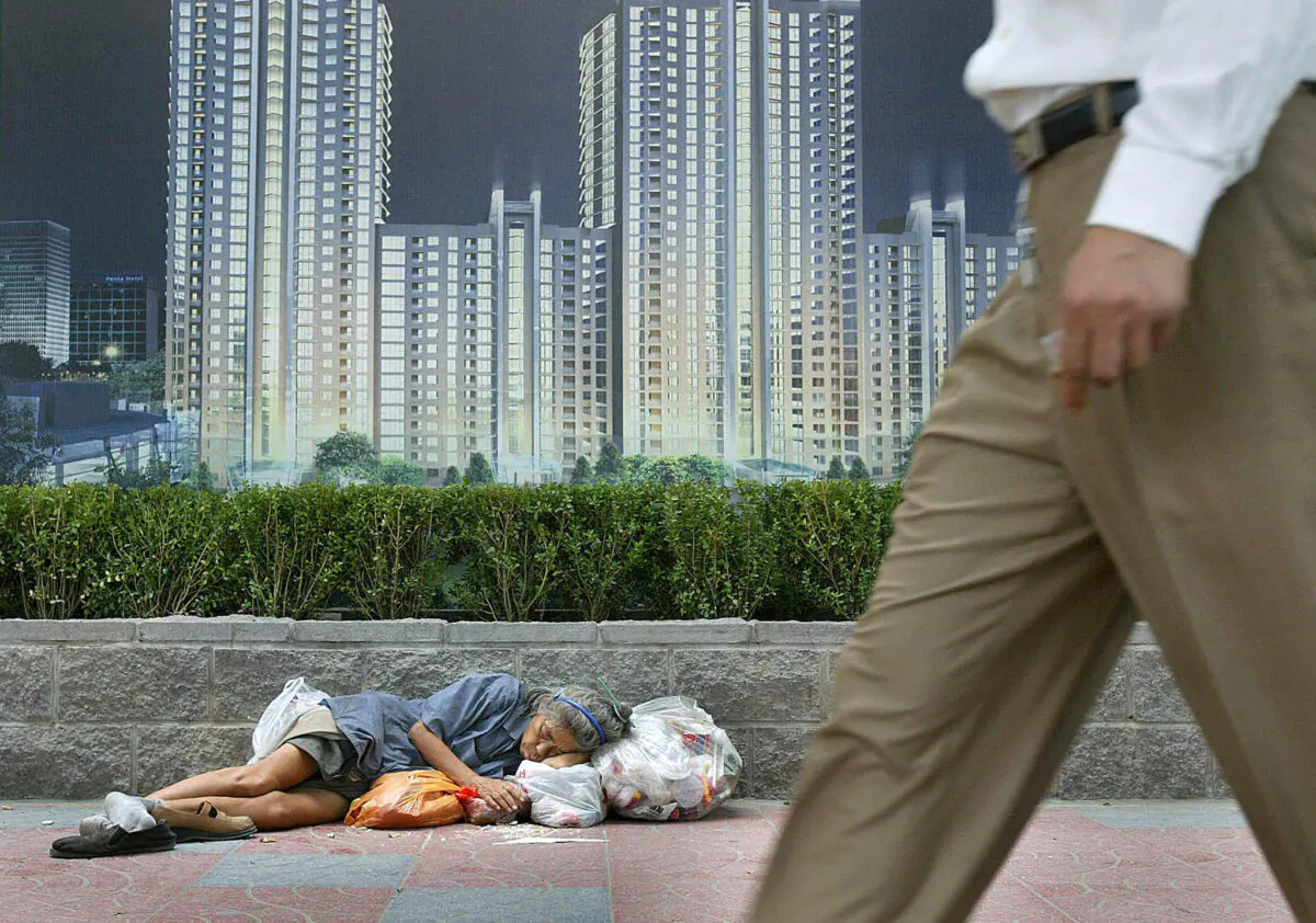 A homeless woman sleeps with her belongings beneath an advertising billboard promoting new urban development in Beijing on Aug. 21, 2003. (Frederic J. Brown/AFP via Getty Images)