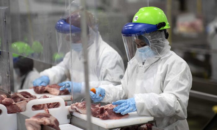 Workers inside Smithfield Foods' Sioux Falls, S.D., pork processing plant wear protective gear and are separated by plastic partitions as they carve up meat on May 20, 2020. (Courtesy Smithfield Foods via AP)