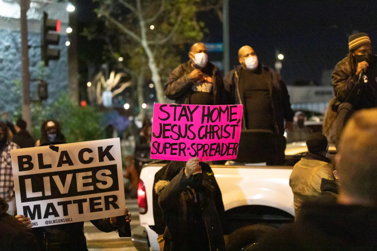 Protesters hold up signs protesting a Christian homeless outreach event while blocking traffic at Skid Row in Los Angeles on Dec. 30, 2020. (John Fredricks/The Epoch Times)