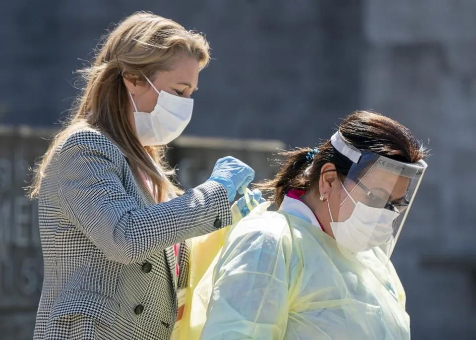 Two health care workers gown up on the sidewalk before going in to Meighen Manor seniors home in Toronto, on April 20, 2020. (The Canadian Press/Frank Gunn)