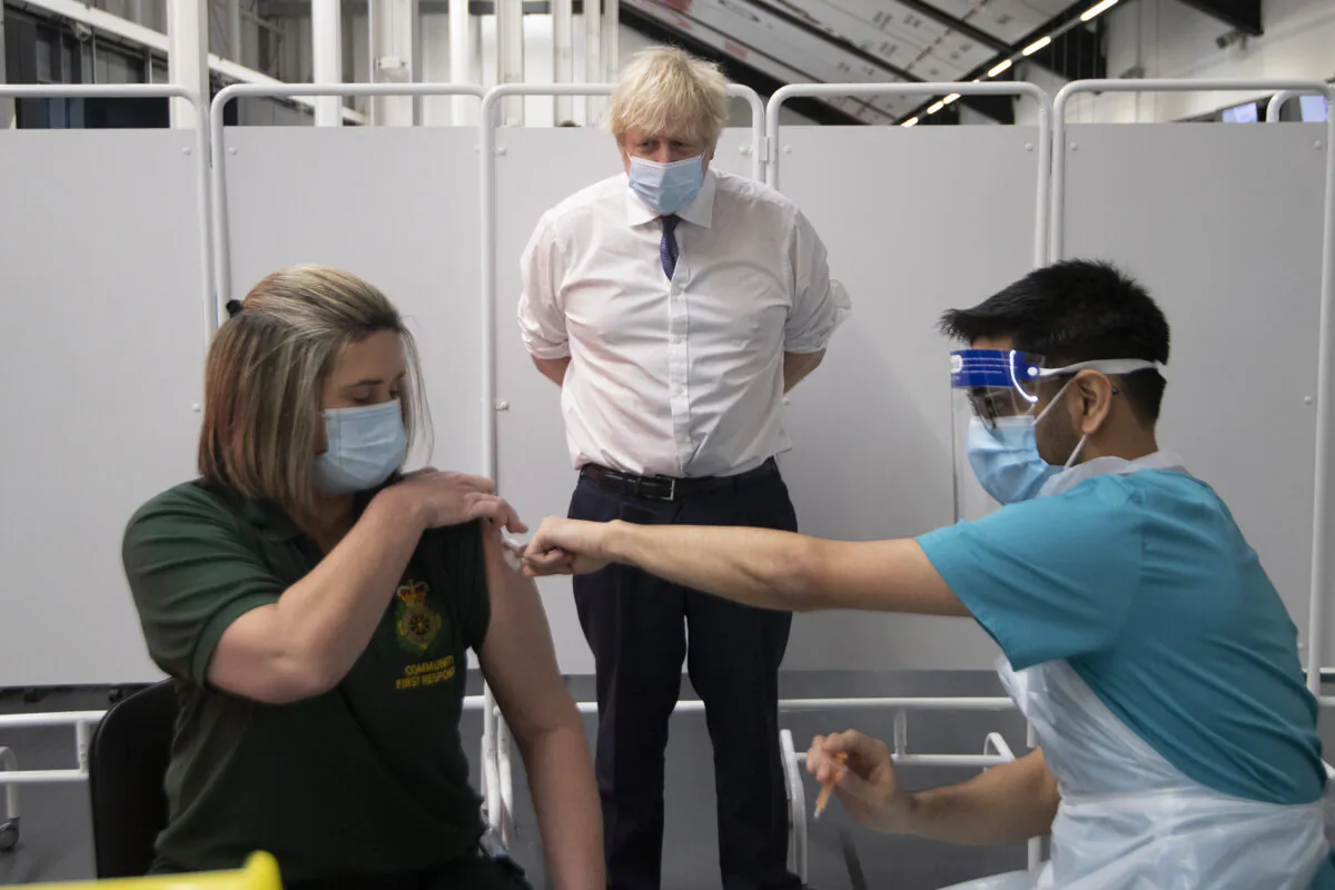 Prime Minister Boris Johnson watches first responder Caroline Cook getting her vaccination as he visits a vaccination centre at Ashton Stadium in Bristol, England, on Jan. 11, 2021. (Eddie Mulholland/WPA Pool/Getty Images)