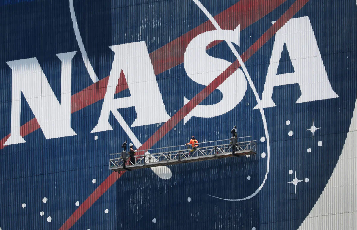 Workers freshen up the paint on the NASA logo on the Vehicle Assembly Building before the arrival of NASA astronauts Bob Behnken and Doug Hurley at the Kennedy Space Center in Cape Canaveral, Fla., on May 20, 2020. (Joe Raedle/Getty Images)