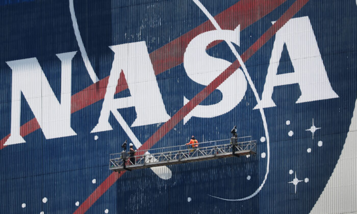 Workers freshen up the paint on the NASA logo on the Vehicle Assembly Building before the arrival of NASA astronauts Bob Behnken and Doug Hurley at the Kennedy Space Center in Cape Canaveral, Fla., on May 20, 2020. (Joe Raedle/Getty Images)